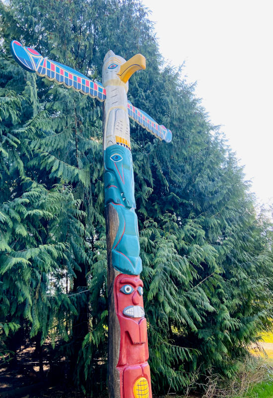 Bunter Totempfahl vor grünen Bäumen im Hintergrund.