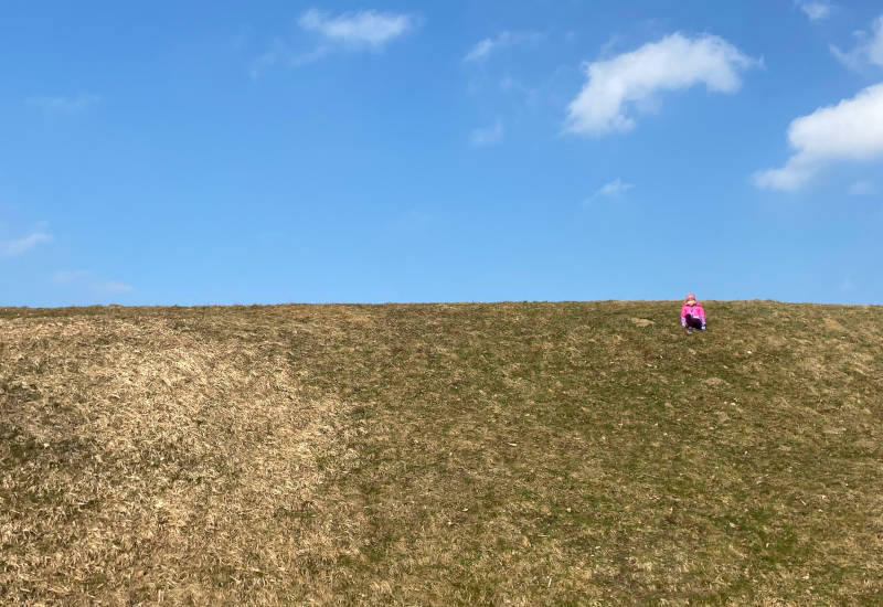 Ein Kind sitzt auf einer grünen Wiese unter blauem Himmel.