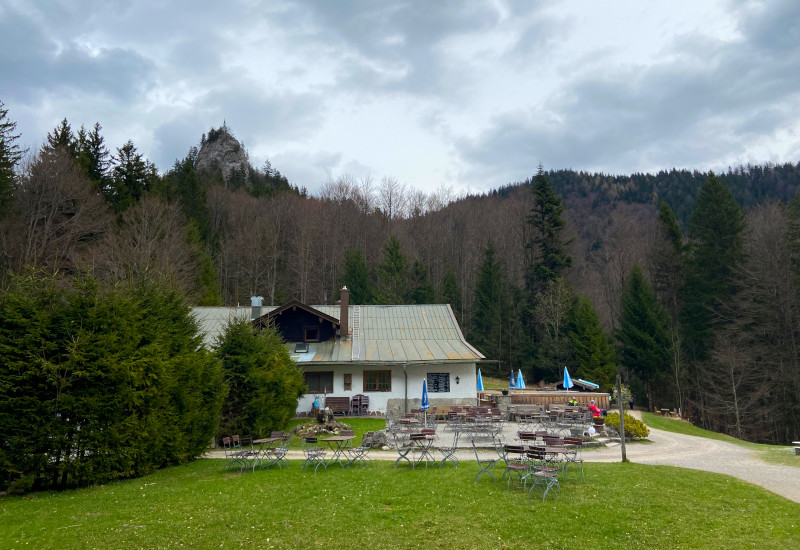 Berggasthaus mit Terrasse, umgeben von Bäumen und Felsen.