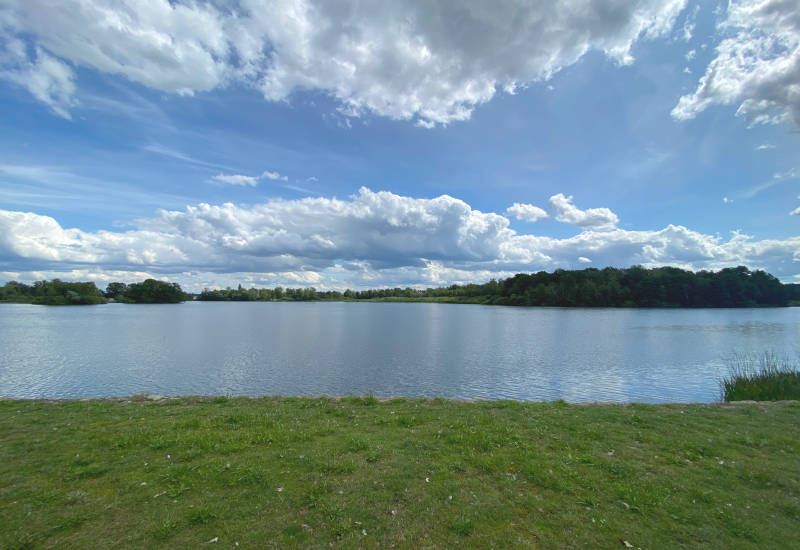 See mit grünem Ufer und bewölktem Himmel.