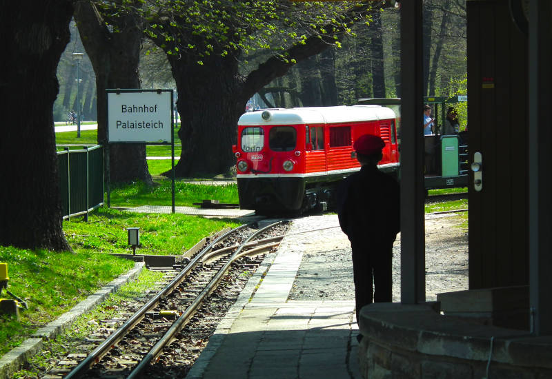 Roter Zug am Bahnhof Palaisteich mit wartendem Person.