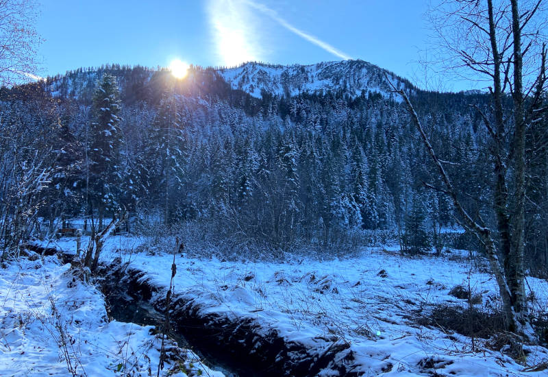 Schneebedeckte Landschaft mit Bergen und Sonnenaufgang im Hintergrund.