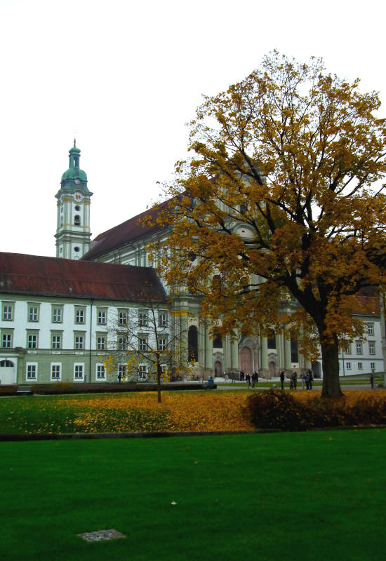 Herbstliche Landschaft mit Kirche, Baum und grüner Wiese.
