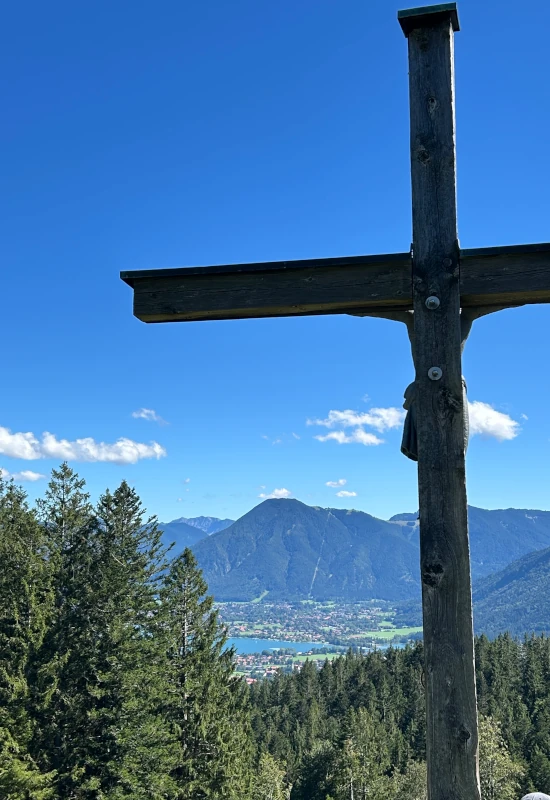 Holzkreuz vor Berglandschaft und blauem Himmel.
