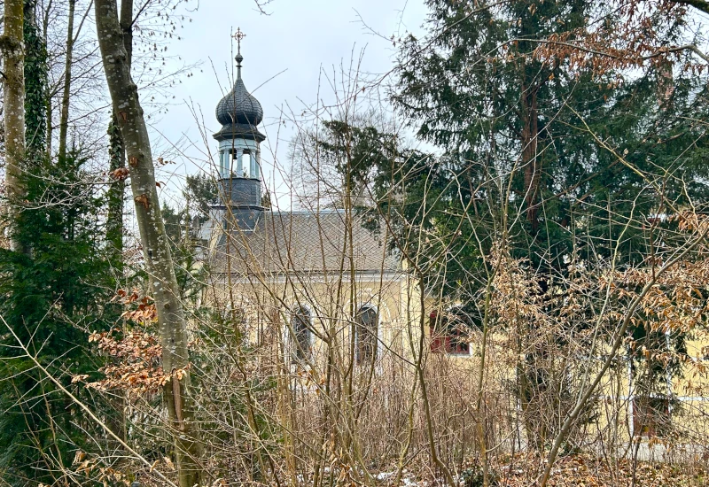 Kirche hinter Bäumen in einer winterlichen Landschaft.